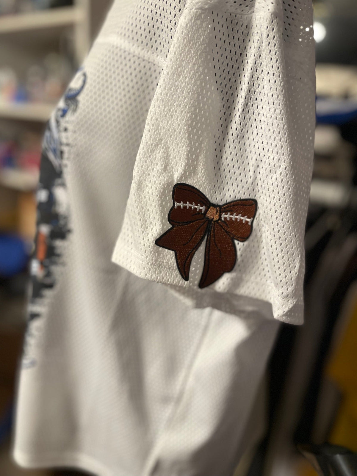 Sleeve of a white custom football jersey with an embroidered football bow patch