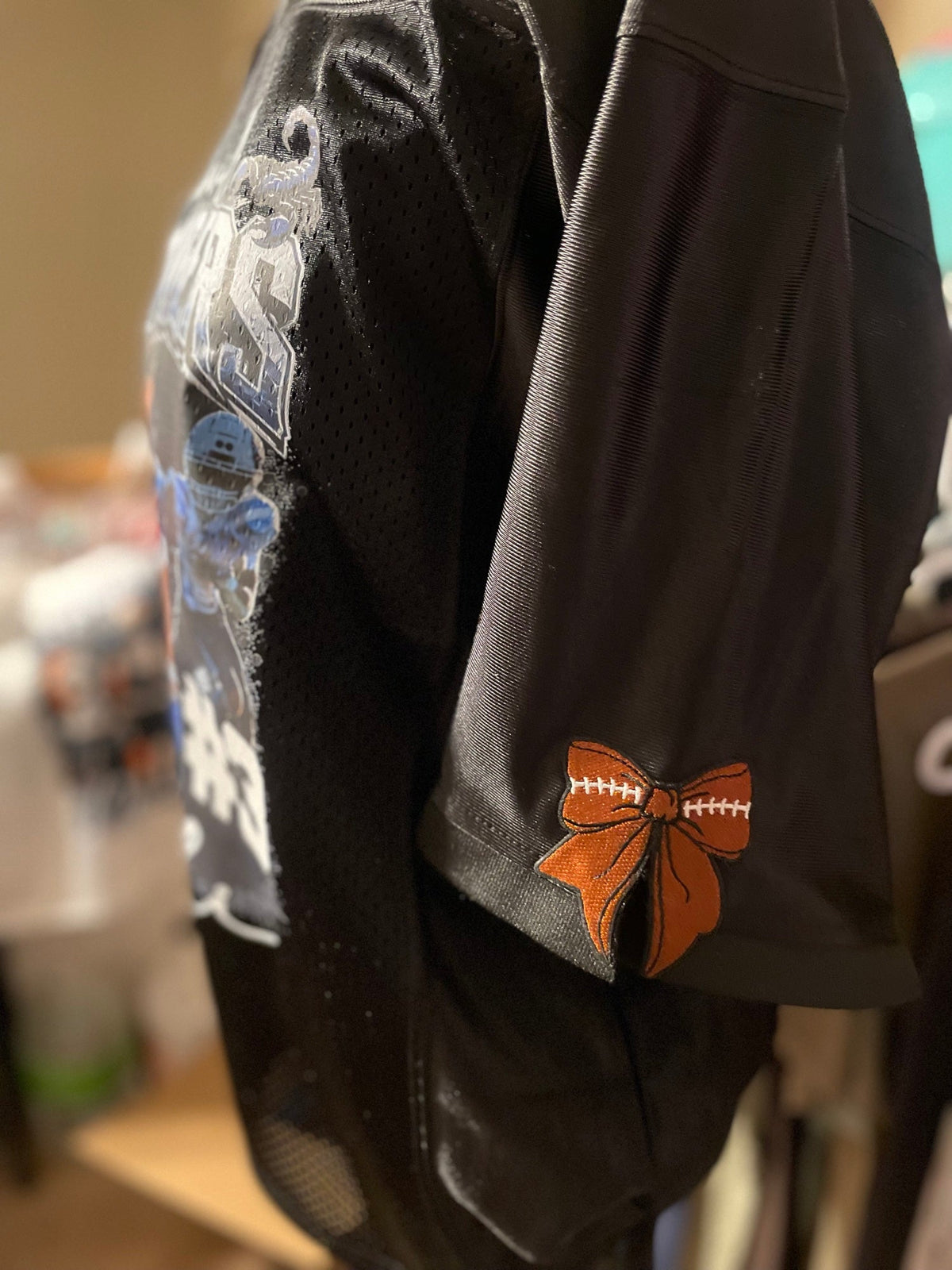 Sleeve of a black custom football jersey with an embroidered football bow patch